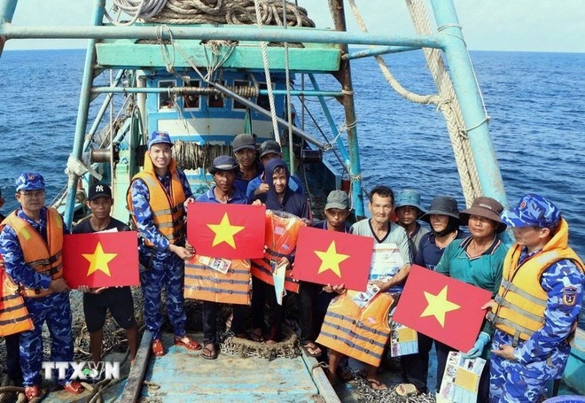 Lực lượng chức năng tặng cờ Tổ quốc, áo phao cho ngư dân trên biển. (Ảnh: TTXVN)