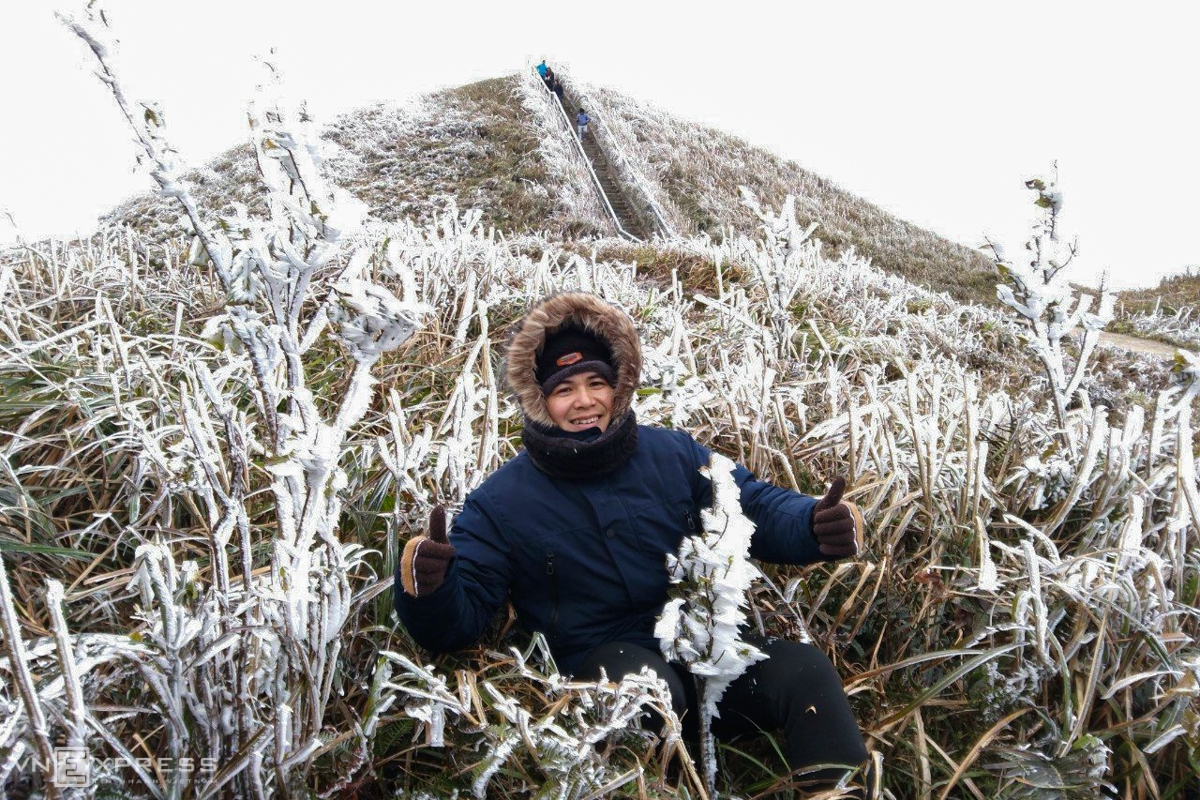 Frost gives Vietnam's northern provinces a new look A tourist takes a check-in photo amidst the frosted grass. Given the strong cold, the man is all bundled up in a thick layer of coats (Photo: VNE)