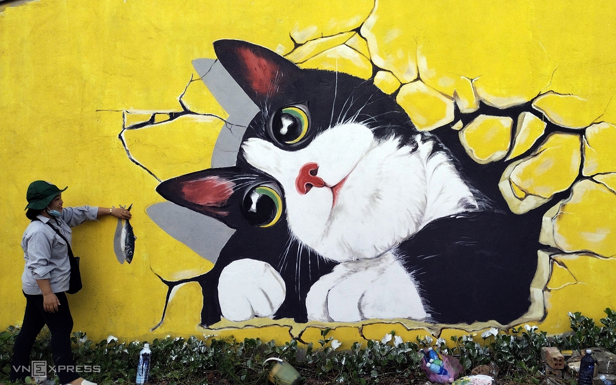 A visitor takes a picture of the hand-painting fish feeding cats on the wall. A visitor takes a picture of the hand-painting fish feeding cats on the wall.