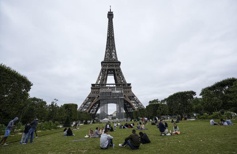 People relax at the Champ-de-Mars garden next to the Eiffel Tower in Paris, Friday, July 16, 2021. The Eiffel Tower is reopening Friday for the first time in nine months, just as France faces new virus rules aimed at taming the fast-spreading delta variant. The Eiffel Tower Reopens After Nine-Month Closure, With Covid Passes Required