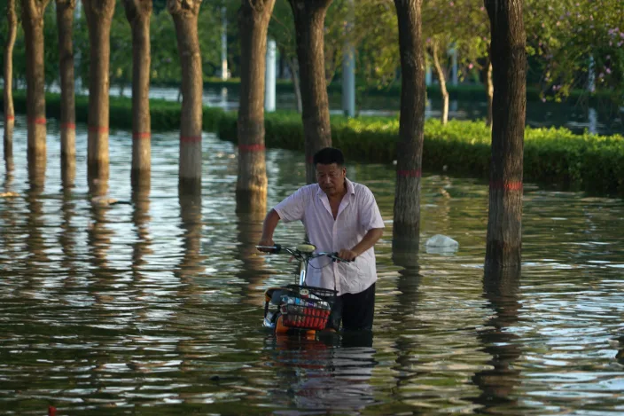 In this July 26, 2021, file photo, a man pushes a scooter through floodwaters in Xinxiang in central China's Henan Province, Monday, July 26, 2021. Chinese authorities have announced a huge jump in the death toll from recent floods. The Henan province government said Monday, Aug. 2, 2021, that over 300 have people died and at least 50 remain missing. (AP Photo/Dake Kang, File) In this July 26, 2021, file photo, a man pushes a scooter through floodwaters in Xinxiang in central China's Henan Province, Monday, July 26, 2021. Chinese authorities have announced a huge jump in the death toll from recent floods. The Henan province government said Monday, Aug. 2, 2021, that over 300 have people died and at least 50 remain missing. (AP Photo/Dake Kang, File)