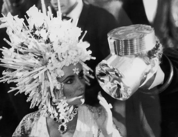 Elizabeth Taylor in a headdress of silver spikes, orchids and lilies chats to designer Cardin, who is wearing what looks like an aluminium gas mask. Photograph: Three Lions/Getty Images 4322 artist
