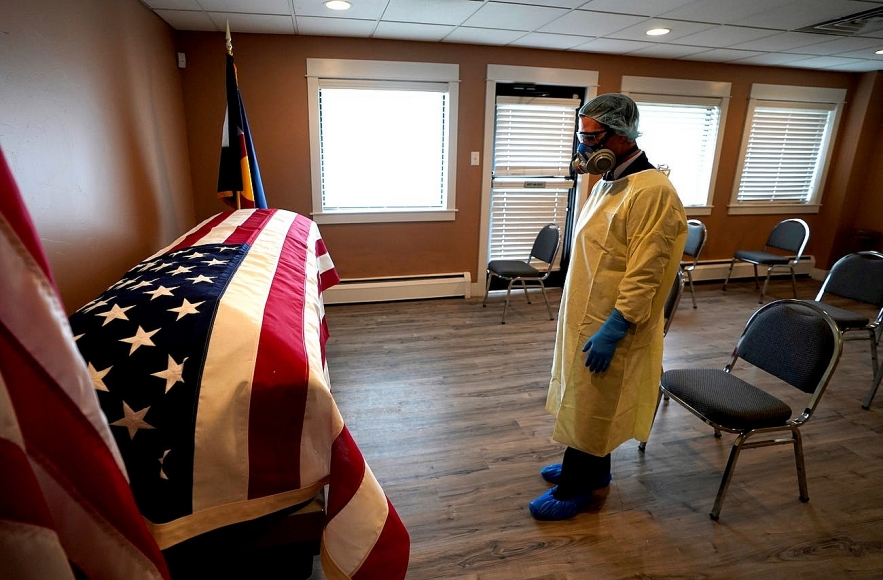 Michael Neel, funeral director of of All Veterans Funeral and Cremation, wearing full PPE, looks at the U.S. flag on the casket of George Trefren, a 90 year old Korean War veteran who died of the coronavirus disease (COVID-19) in a nursing home, in Denver, Colorado, April 23, 2020. Rick Wilking/Reuters 2200 us covid