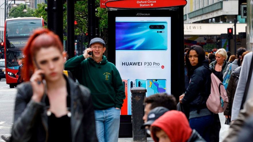 Pedestrians use their mobile phones near a Huawei advert at a bus stop in central London last year. Photo: AFP. 5716 huawei 2