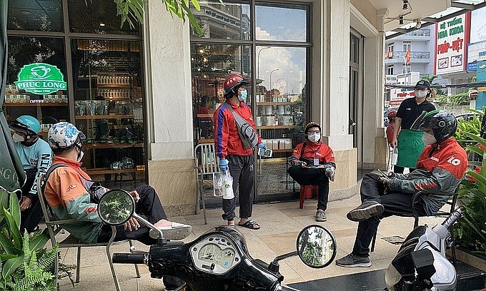 Shippers wait outside a coffee shop for their customers' takeaway drinks in downtown HCMC, October 2021. Photo: VnExpress Shippers wait outside a coffee shop for their customers' takeaway drinks in downtown HCMC, October 2021. Photo: VnExpress