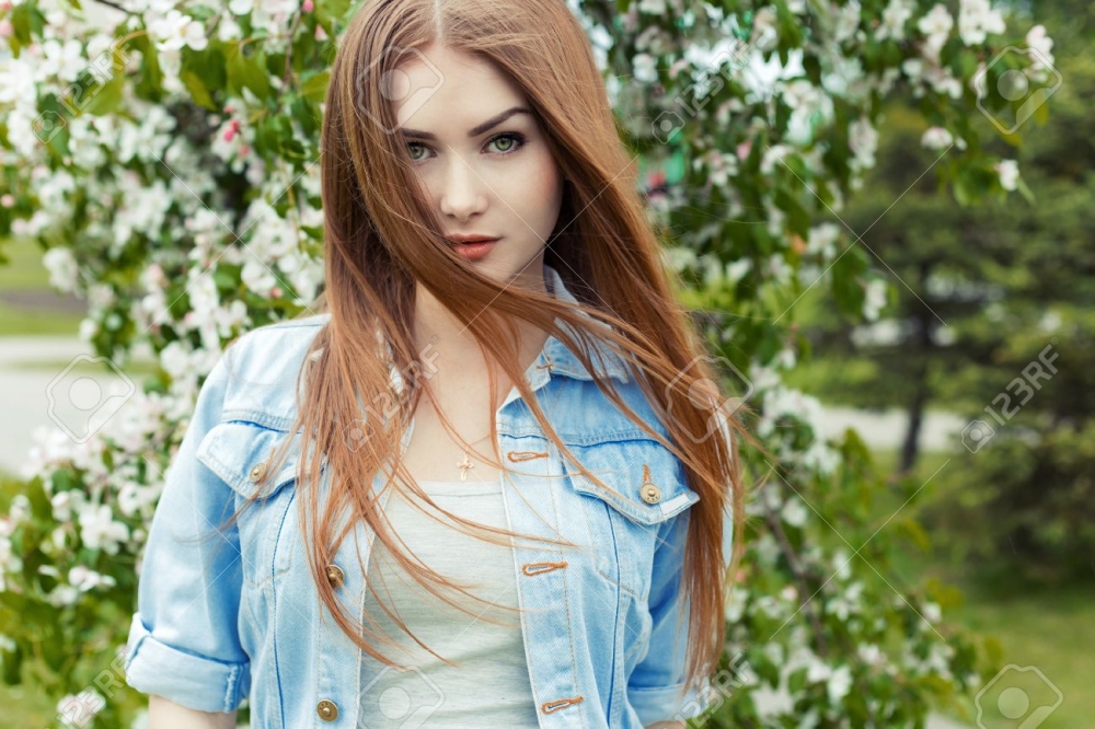 undefined 0219 41733034 beautiful sexy cute sweet girl with long red hair and green eyes in a denim jacket near a flowering